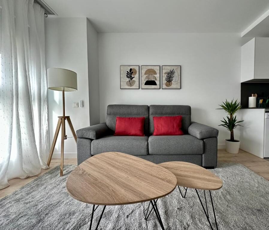 Szara sofa z dwoma czerwonymi poduszkami przed drewnianymi, zagnieżdżonymi stolikami kawowymi